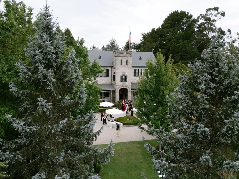 Historic stone mansion viewed through flowering trees, with manicured grounds and a courtyard entrance